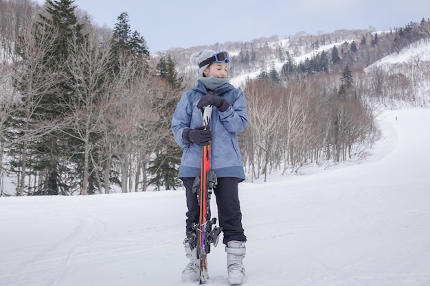 Mujer con esquí en la mano con gafas de esquí en la montaña de invierno de nieve.