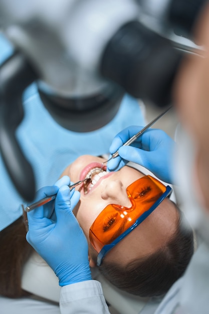 La mujer está acostada en la silla dental bajo el microscopio mientras el dentista la examina con espejo y explorador