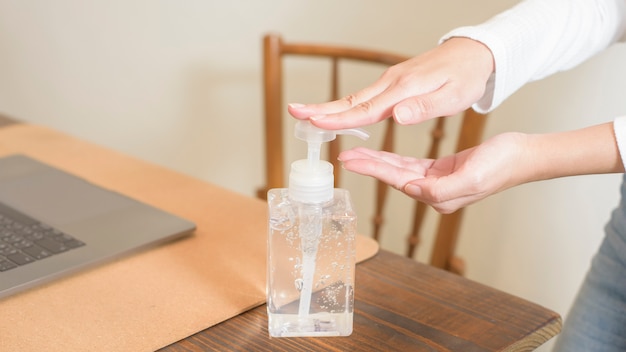 La mujer está aplicando gel desinfectante a las manos en la mesa de trabajo