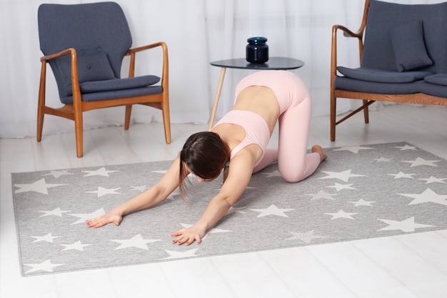 La mujer está arrodillada en una pose de gato con los brazos extendidos y haciendo un estiramiento de espalda