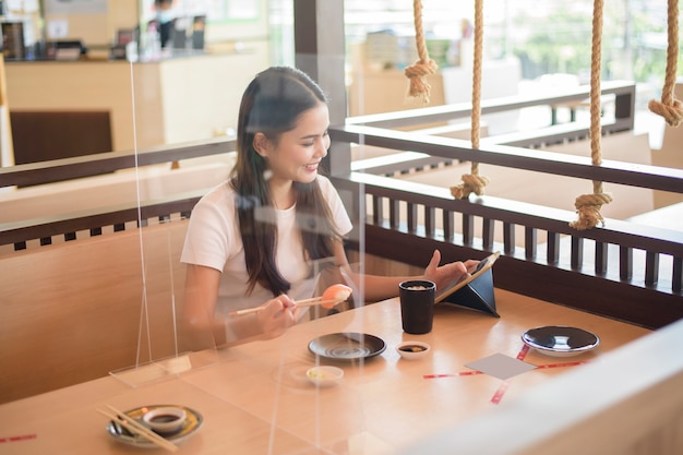 La mujer está comiendo en un restaurante con protocolo de distanciamiento social durante el cierre de la ciudad debido a la pandemia de coronavirus