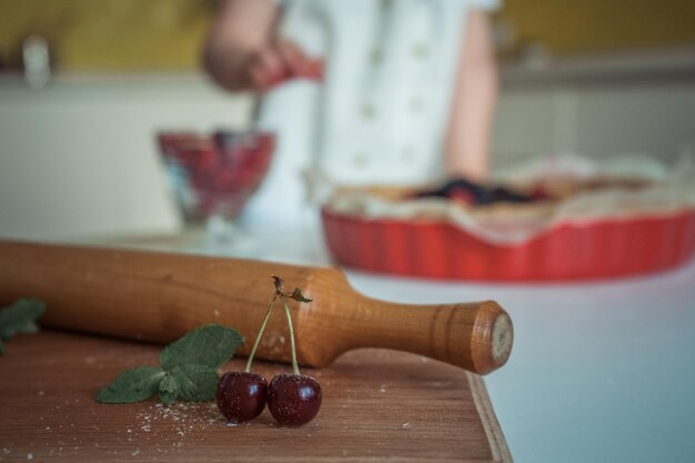 Una mujer está cortando un pastel de cerezas con un rodillo.