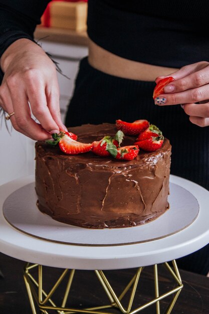 Una mujer está cortando un pastel de chocolate con fresas encima.