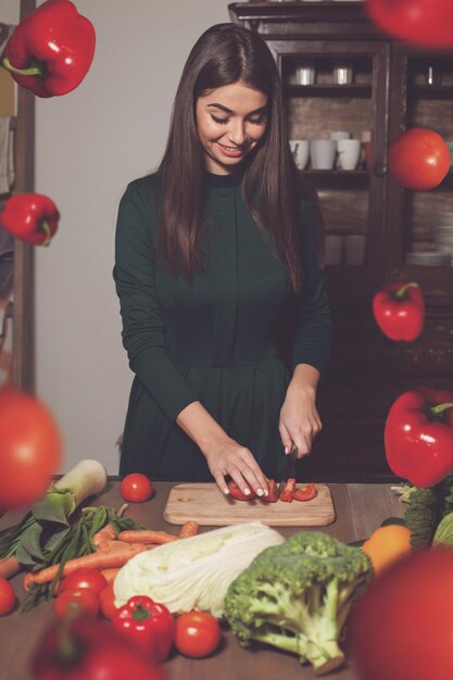 La mujer está cortando tomates en la mesa con muchas verduras diferentes