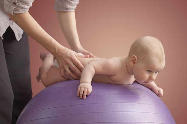 La mujer está dando masajes a su bebé en una bola púrpura. Fondo de color.