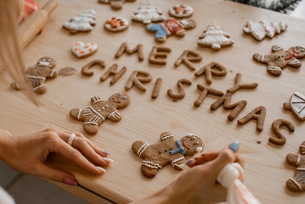 La mujer está decorando a un hombre de pan de jengibre tradicional. Las letras para hornear componen las palabras de feliz Navidad.