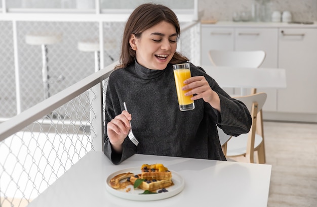 Una mujer está desayunando con gofres belgas y jugo de naranja.