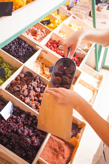 La mujer está empacando albaricoques secos en la tienda de comestibles. Frutos secos en las cajas de madera, comida vegana.