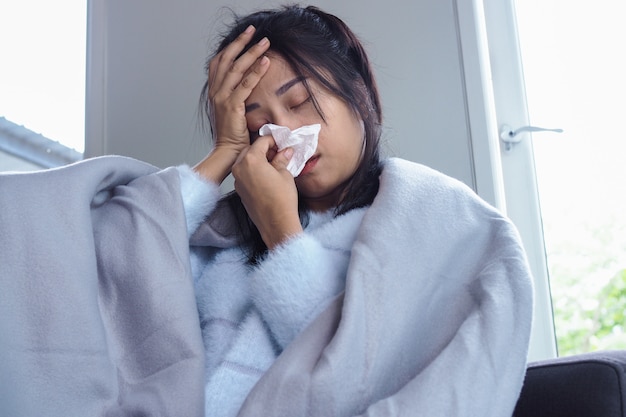 La mujer está enferma con dolor de cabeza, fiebre alta y gripe, sentada debajo de una manta