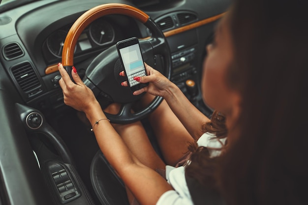 La mujer está enviando mensajes de texto en un teléfono inteligente mientras conduce un automóvil y se pone en peligro.