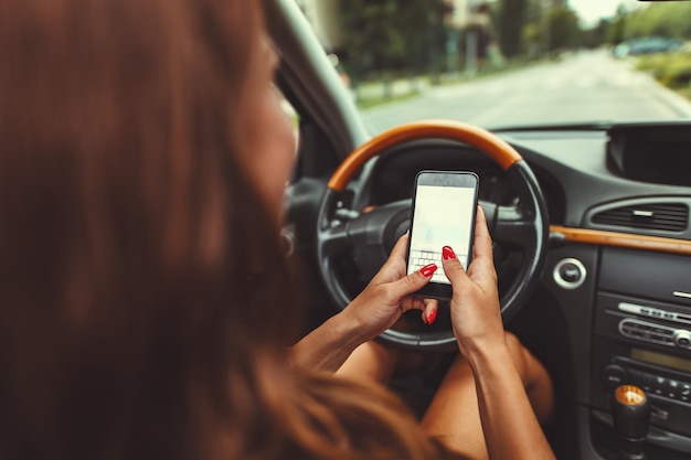La mujer está enviando mensajes de texto en un teléfono inteligente mientras conduce un automóvil y se pone en peligro.