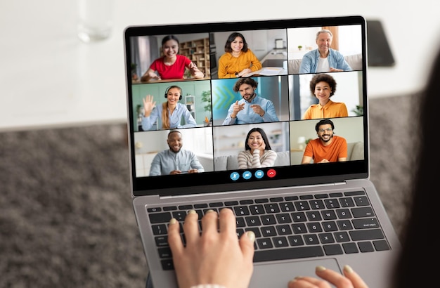 Una mujer está escribiendo en una computadora portátil participando en una videoconferencia con otras ocho personas