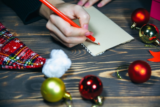 La mujer está escribiendo postales de Navidad. Saludos con fiestas. Feliz año nuevo. Felicitaciones a amigos y familiares. Decoraciones de mesa de madera. Ambiente acogedor. Copie el lugar del espacio.