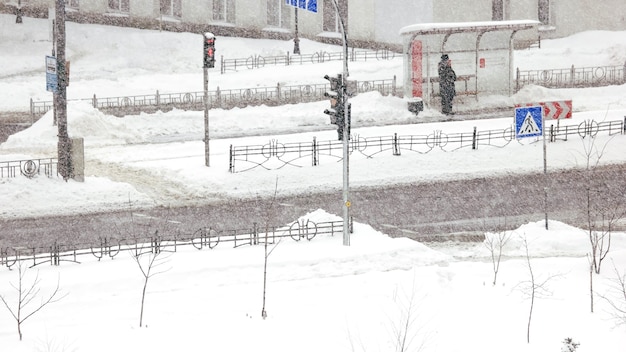 La mujer está esperando el autobús durante la tormenta de nieve. Carretera de la ciudad durante una fuerte tormenta de nieve en invierno. Malas condiciones climáticas invernales. Escena urbana de la vida de la ciudad en invierno.