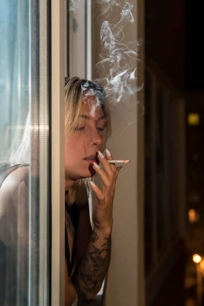 La mujer está fumando un cigarrillo por la noche junto a la ventana