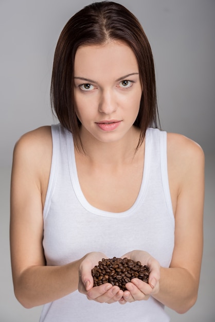Mujer está mostrando puñado de granos de café tostado.