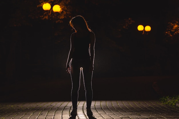 La mujer está parada en el callejón oscuro. Noche