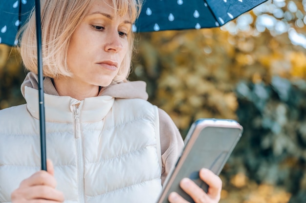 La mujer está en el parque de otoño con un paraguas y un teléfono Atmósfera otoñal