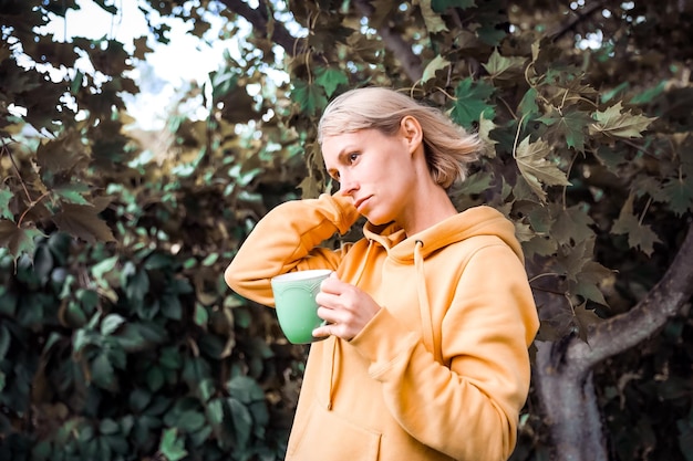 La mujer está en el parque de otoño con una taza de té Atmósfera de otoño