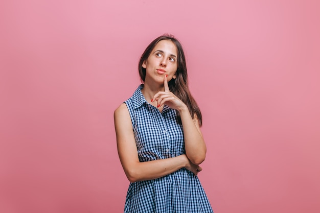 La mujer está pensando y sosteniendo su cabeza en una pared rosa.