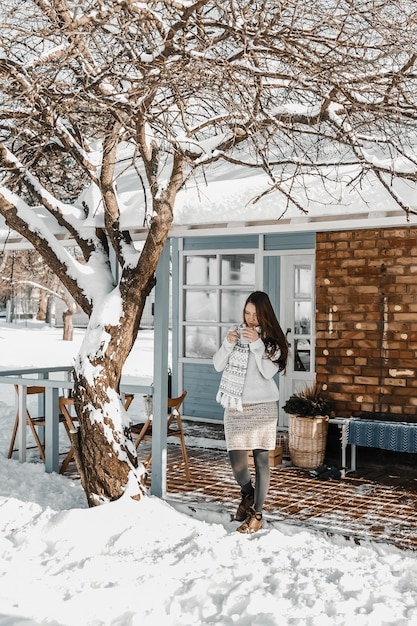 La mujer está de pie en una casa en invierno por la mañana y está bebiendo té caliente.