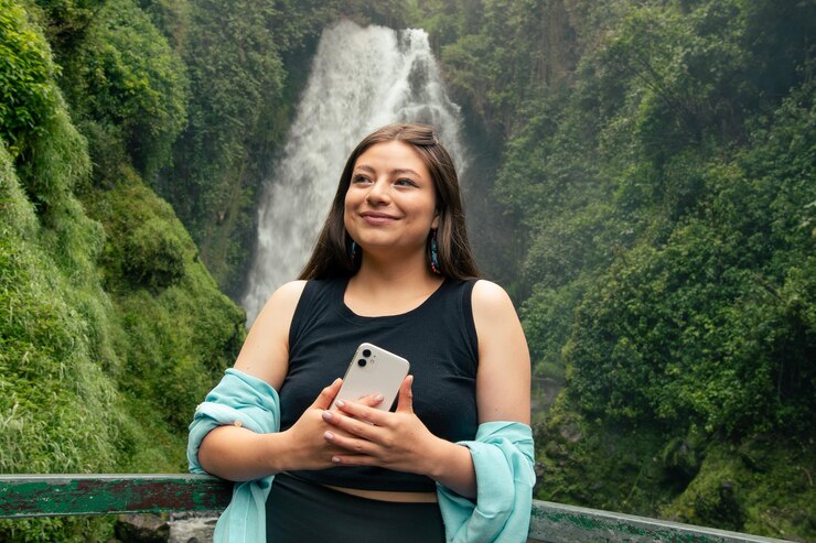Foto una mujer está de pie frente a una cascada y sostiene un teléfono