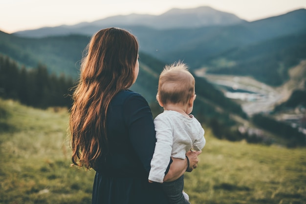 Una mujer está de pie mirando las montañas y sostiene a un niño en sus brazos