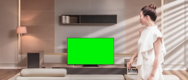 Una mujer está de pie en una sala de estar con un televisor con pantalla verde.