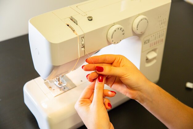 La mujer está poniendo hilo en la máquina de coser Manos de las niñas en el trabajo independiente Concepto de moda Creación de proceso de ropa nueva Ideas de pasatiempo