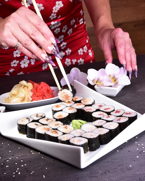 Una mujer está poniendo sushi en un plato con una flor al costado.