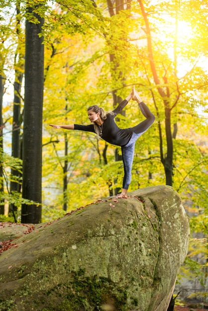 Mujer está practicando yoga en el bosque de otoño en la piedra grande