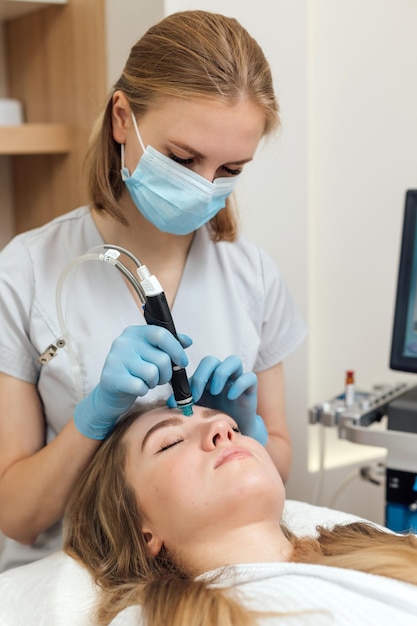 La mujer está recibiendo un tratamiento facial hidratante de rejuvenecimiento de limpieza facial al vacío hidrafacial