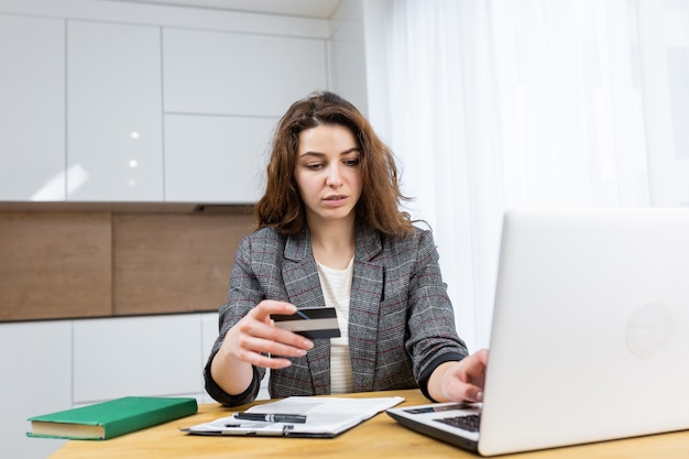 La mujer se está relajando en casa, comprando en línea, usando una computadora portátil y una tarjeta de crédito