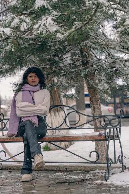 Una mujer está sentada en un banco en la nieve con una bufanda púrpura