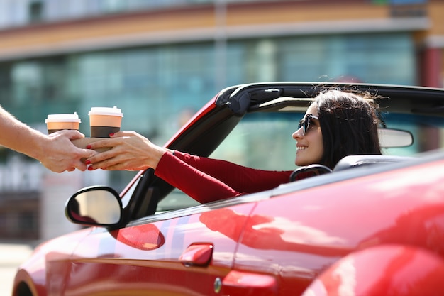 La mujer está sentada en un coche convertible que se sirve en tazas de café