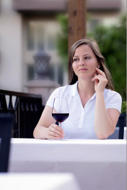 Una mujer está sentada con una copa de vino tinto en un café de verano y sueña con algo