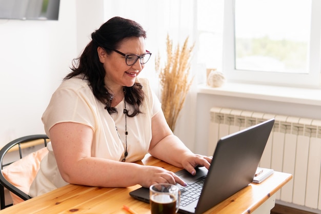 Una mujer está sentada en una habitación en una mesa con una computadora portátil