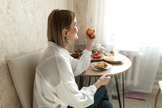 mujer está sentada en una mesa con una manzana en la mano que mira.