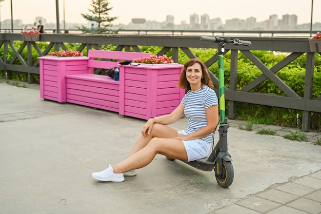 Una mujer está sentada en un scooter en el terraplén de Kazán. Transporte ecológico.