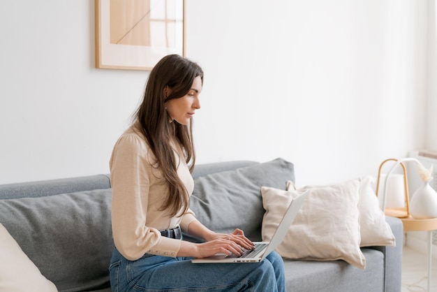 La mujer está sentada en un sofá y escribiendo en una computadora portátil