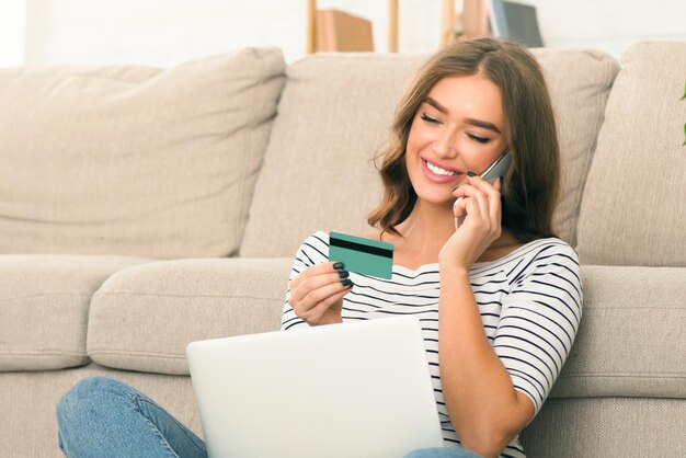 Una mujer está sentada en un sofá participando en una conversación telefónica mientras sostiene una tarjeta de crédito en la mano