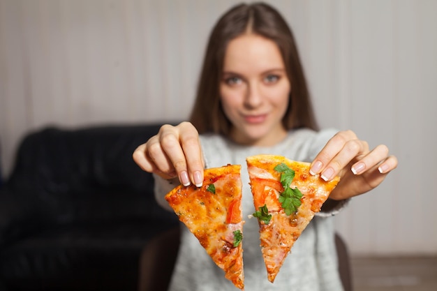 La mujer está sentada y tiene dos rebanadas de pizza en sus manos.