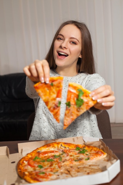 La mujer está sentada y tiene dos rebanadas de pizza en sus manos.