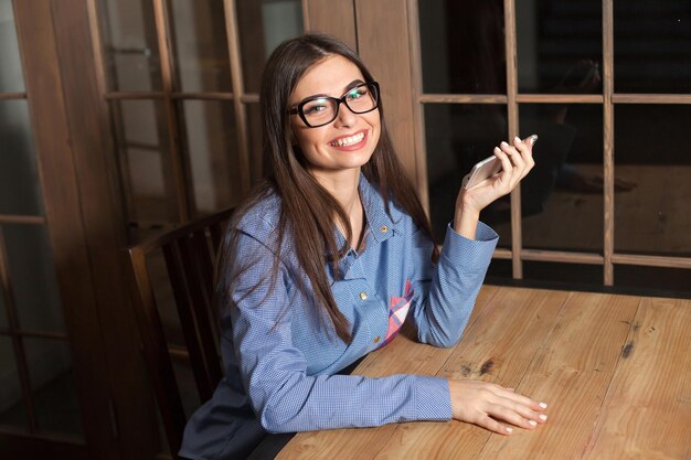 La mujer está sonriendo y sentada en la mesa con el teléfono