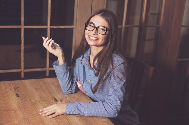 La mujer está sonriendo y sentada en la mesa con el teléfono