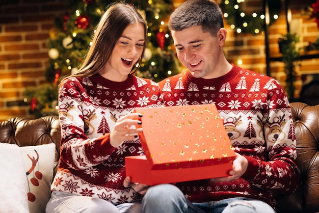 La mujer está sorprendida y emocionada después de abrir la caja de regalo recibida. El hombre feliz está haciendo un regalo de Navidad.