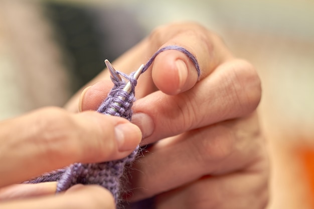 La mujer está tejiendo un suéter azul cálido. Un hobby de anciana está tejiendo.