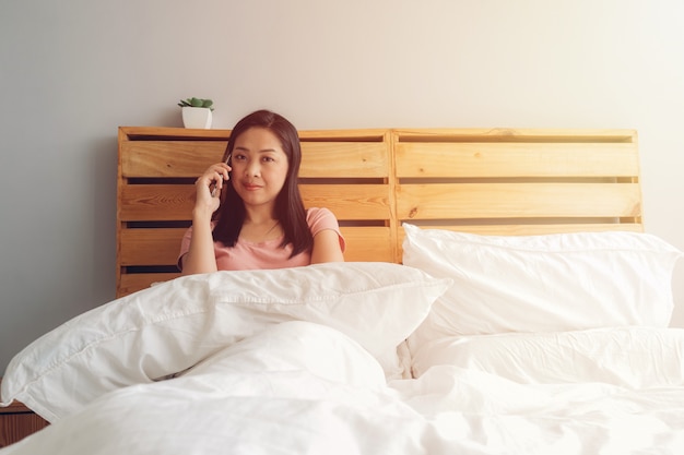 La mujer está teniendo una conversación telefónica en su cama por la mañana.