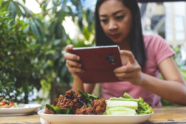 Mujer está tomando una foto de comida tailandesa en la mesa.