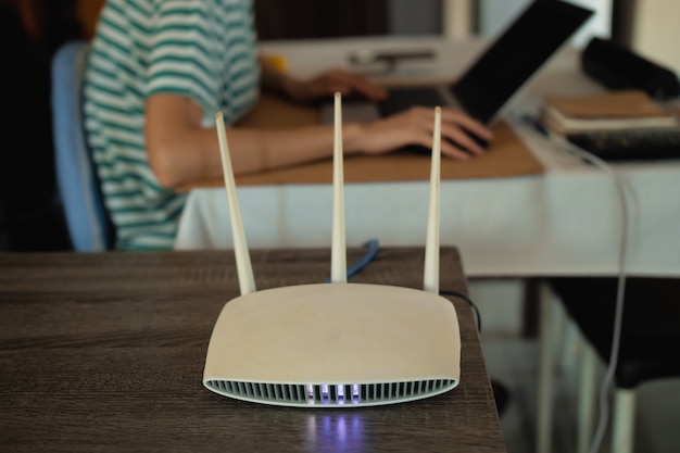 Una mujer está trabajando en casa usando un módem enrutador, conectando Internet a su computadora portátil.